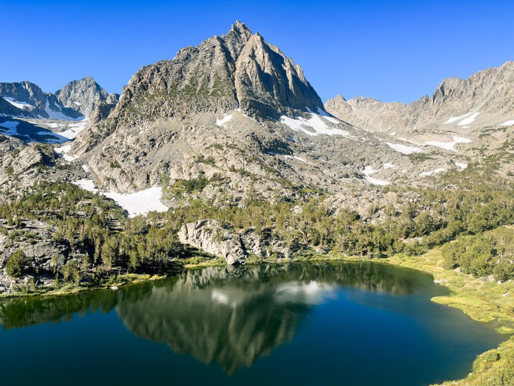 An alpine lake on a hiking trail in california and the mountains towering behind it.