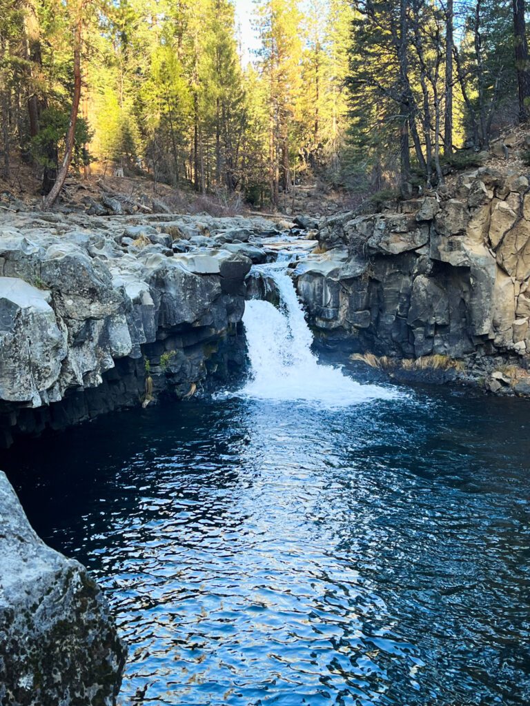 a small waterfall near mount shasta with a large, deep pool and surrounding basalt formations