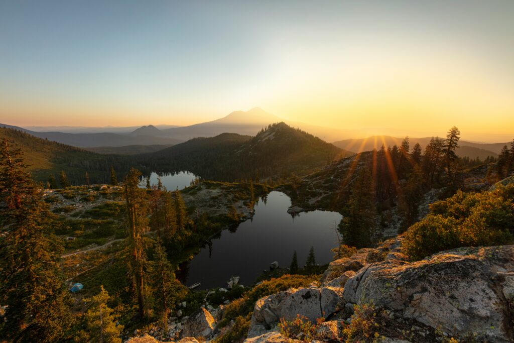 the sun rising above alpine lakes, with mt shasta in the distance