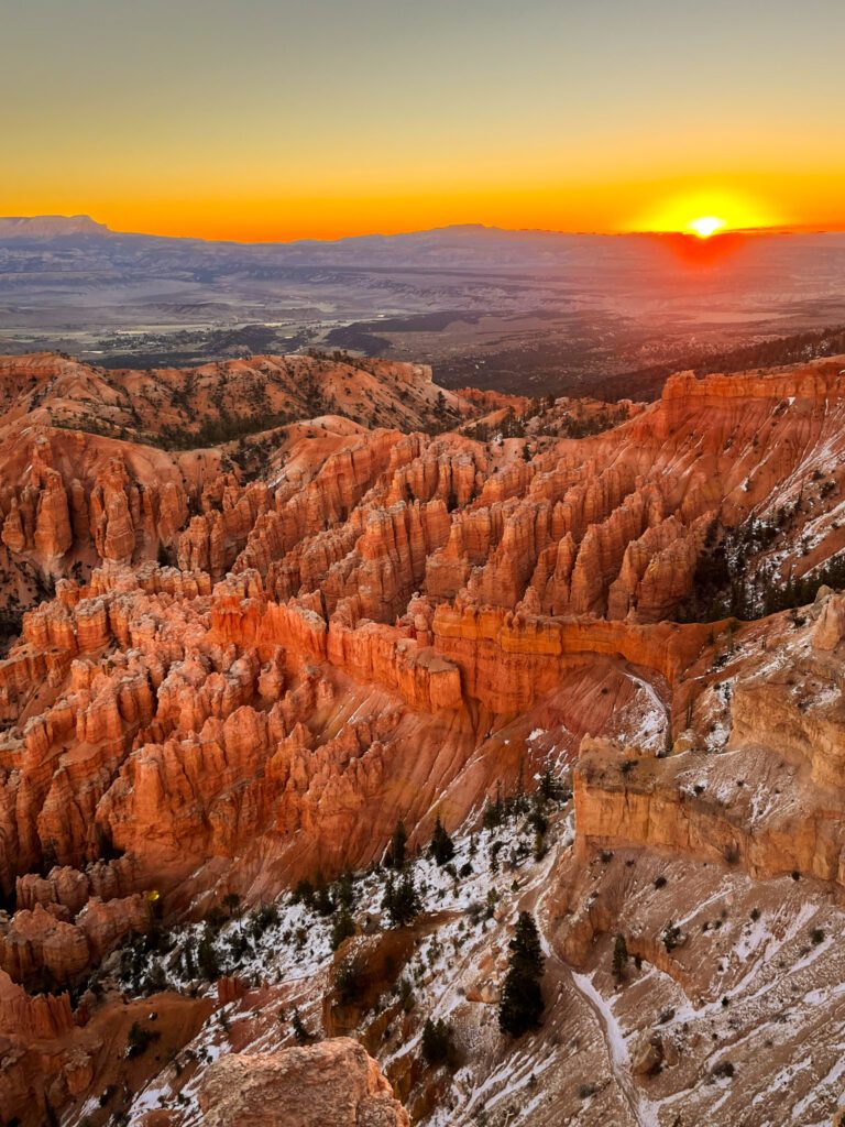 the sun rising behind orange hoodoo formations