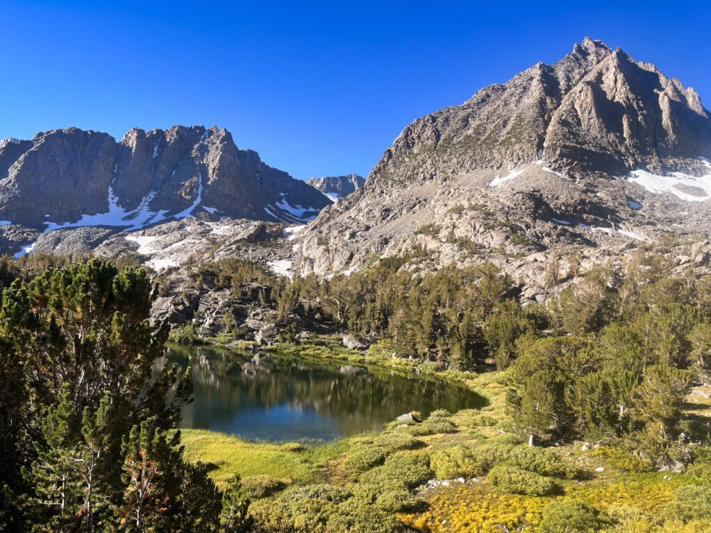 An alpine lake next to a meadow and dramatic mountains.