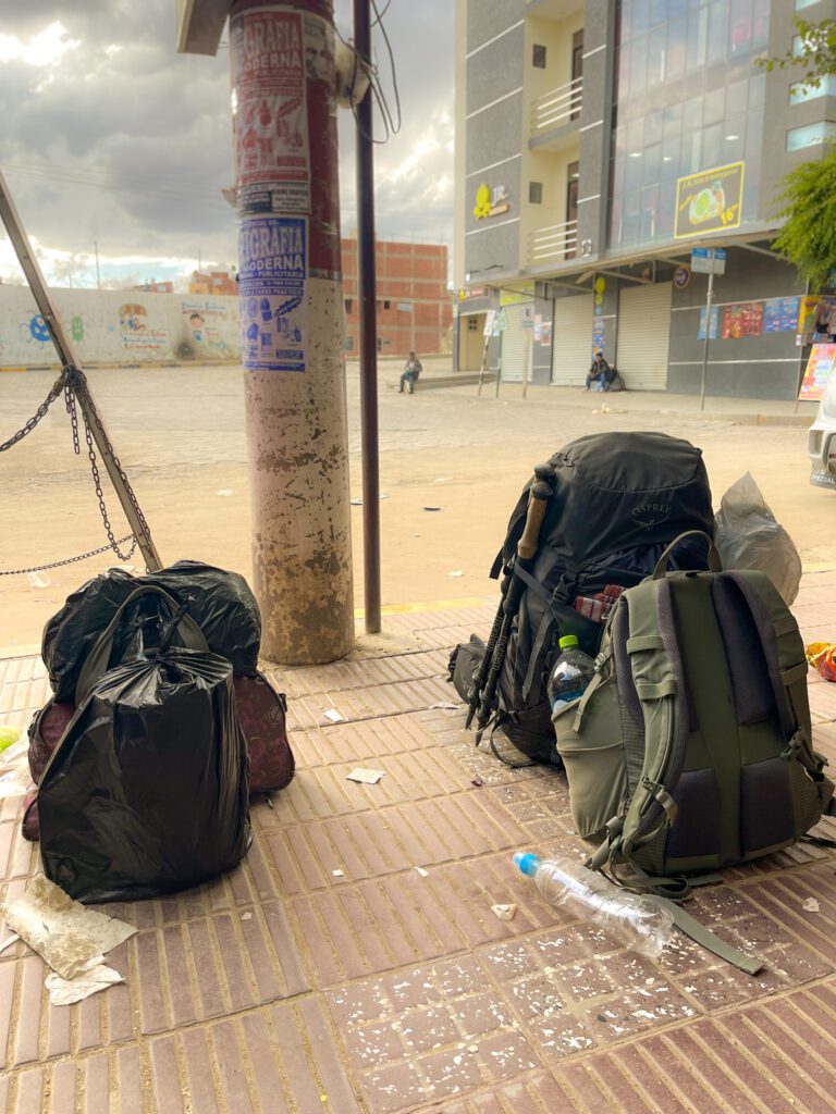 a long-term traveler's backpacks on a dusty sidewalk in a small town with dirt roads.