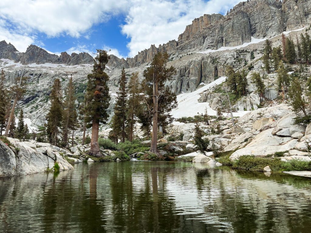 a deep green alpine lake in sequoia national park, with a dramatic rocky lakeshore and tall granite mountains behind it.