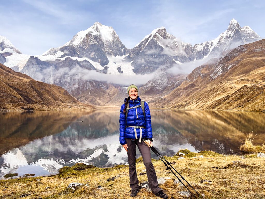 a hiker poses in front of an alpine lake with dramatic snowy mountains.