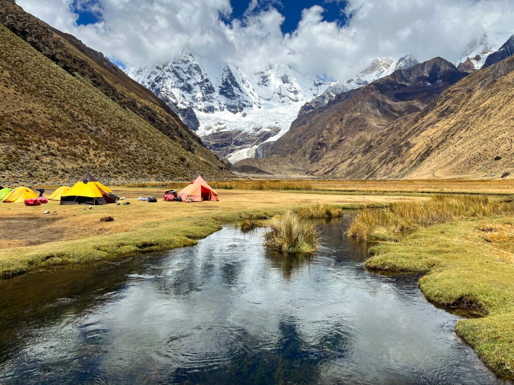 a backpacking campsite next to a river and in front of snowy mountains