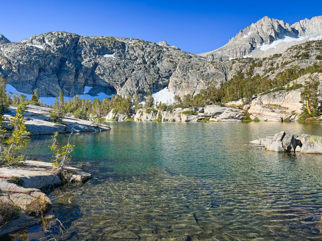 Gem lake, an alpine lake on the little lakes valley hike with turquoise waters and rocky, snowy mountains behind it.