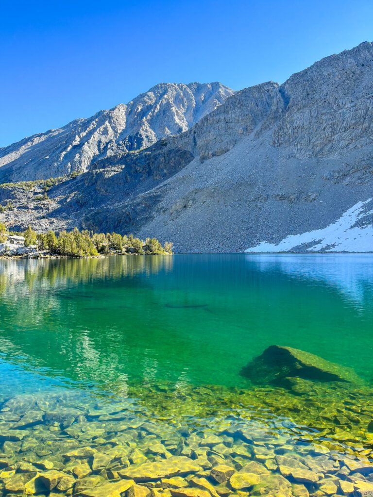 A brightly colored, green-blue alpine lake with clear waters on a hiking trail in california