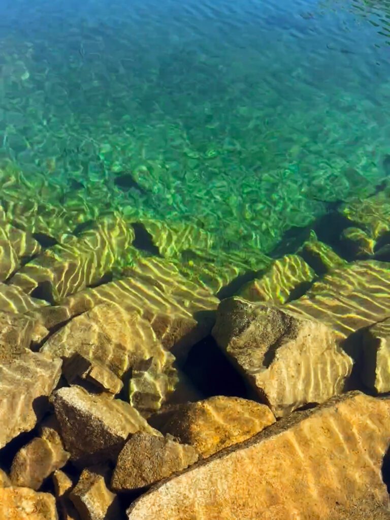 close-up of the pristine turquoise water of an alpine lake in california and the rectangular rocks along the lakeshore.