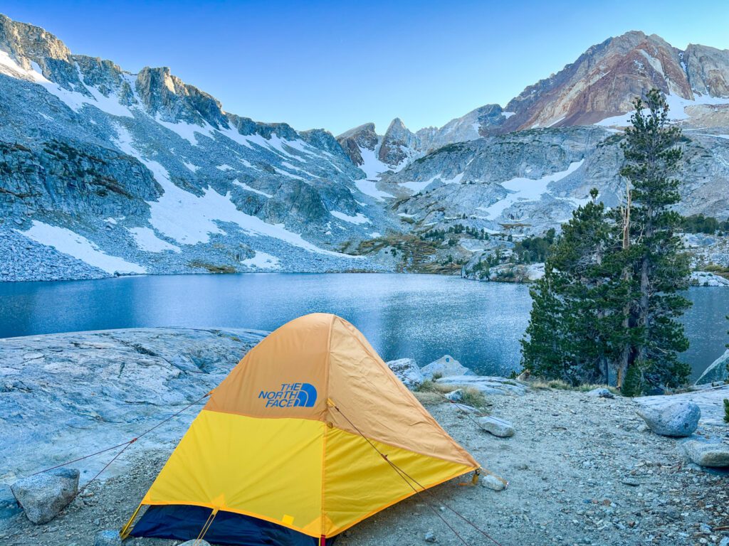 a backpacking tent set up overlooking an alpine lake and the snowy mountains behind it.