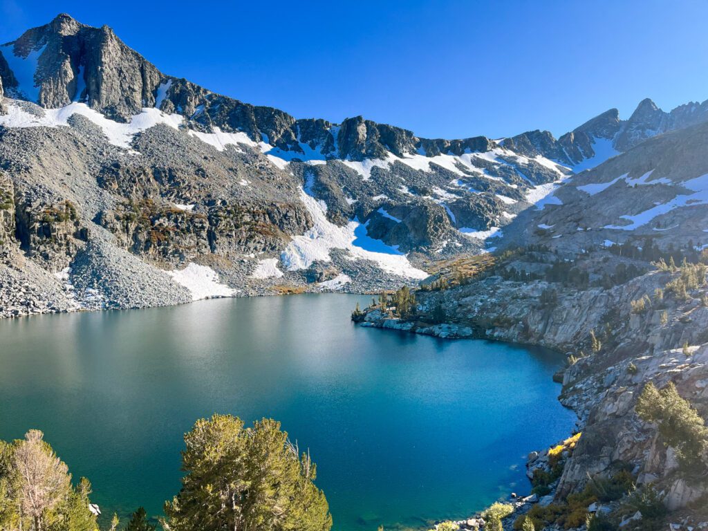a deep blue alpine lake surrounded by a basin of snowy granite mountains, as seen on a california hiking trail