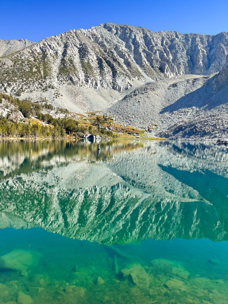 Steelhead lake, a turquoise alpine lake on the big mcgee lake hike that perfectly reflects the craggy peak above it.
