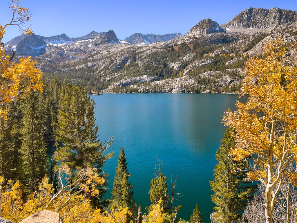 View from South Lake in bishop, california, where the deep sapphire color of the water contrasts with the golden aspens and green conifers surrounding it.