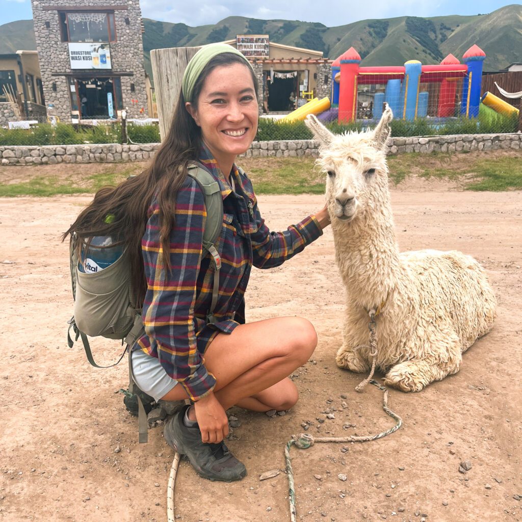 a solo female traveler in a flannel shirt poses next to a llama.