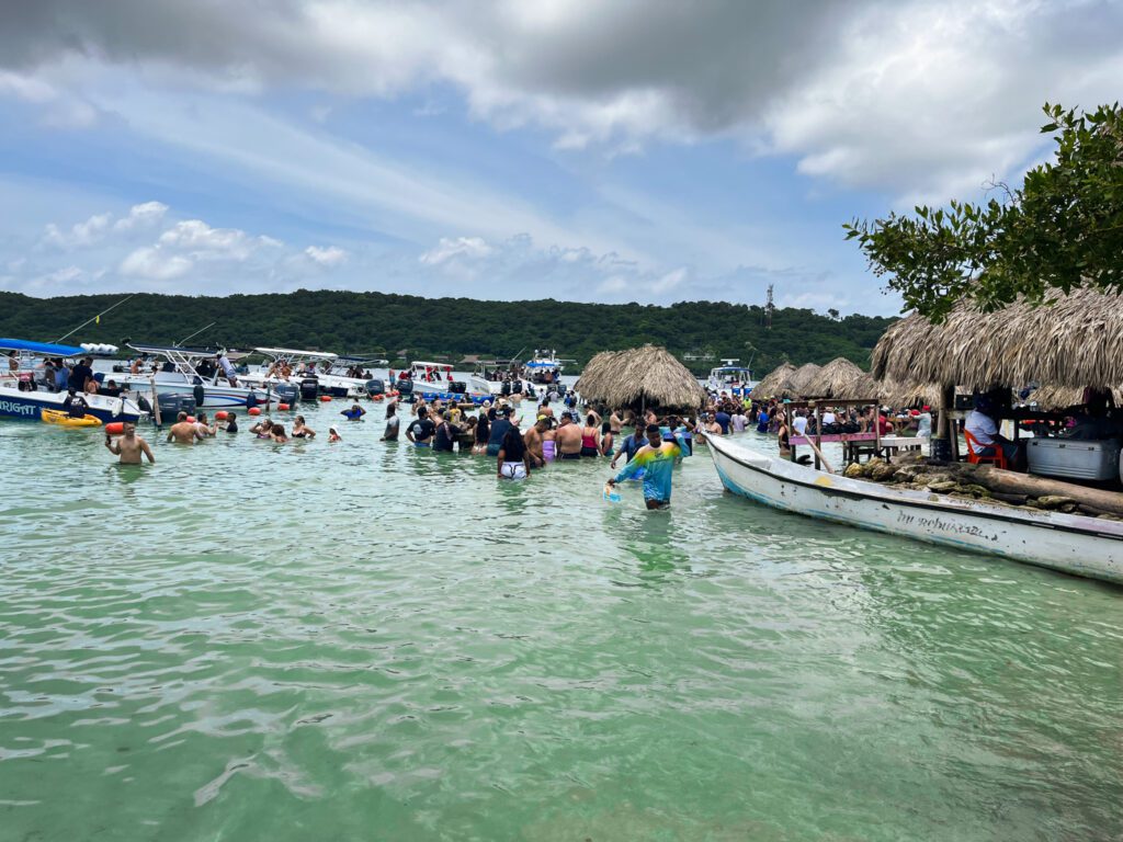a tropical beach area where vendors bring food and drinks to guests at tables in the water