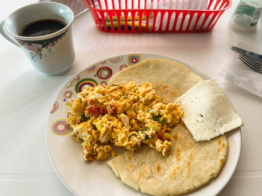 a colombian breakfast of scrambled eggs, arepas, cheese, and coffee
